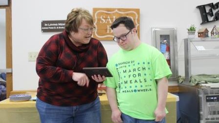 woman holds small rectangular plaque so man in eye glasses can read it.